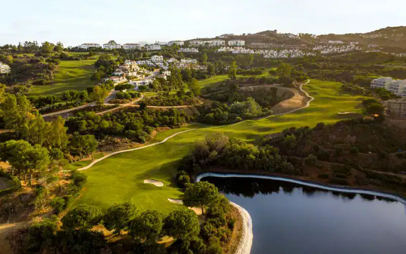 a golf course with a body of water and a town in the background