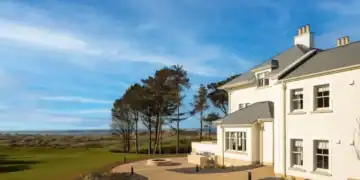 A large white house with a golf course and trees.