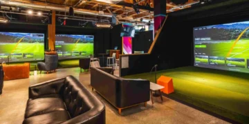 A room with a large golf simulator screen and a couch.