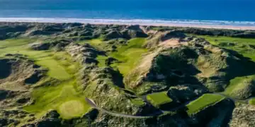 A golf course with the sea and beach in the background.