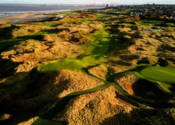 a golf course with sand dunes and water in the background