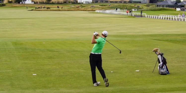 Golfer swings on lush green course.